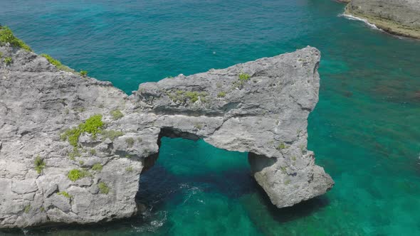 Rock arch cliff surrounded by shallow blue turquoise water, aerial