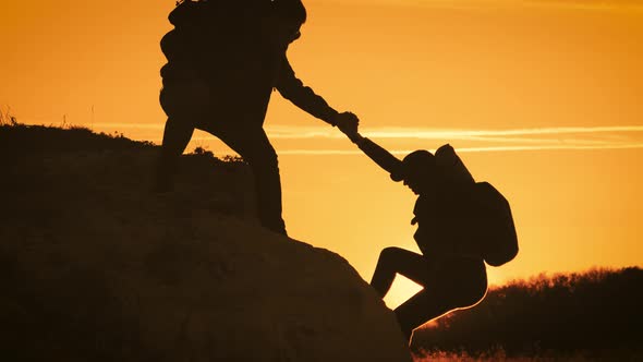 Silhouette of Helping Hand Between Two Climber. Two Hikers on Top of the Mountain, a Man Helps a