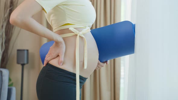 Close up of Asian beautiful pregnant woman hold exercise mat in house.