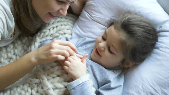 smiling lady with fair hair talks to kid and touches nose alt