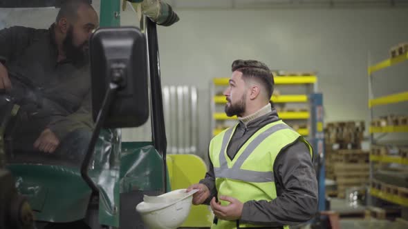 Profile Portrait of Young Bearded Caucasian Man Putting on Helmet and Talking To His Colleague in
