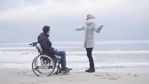 Cheerful Caucasian Woman Talking with Boy in Wheelchair and Pointing Away. Adult Mother and Young