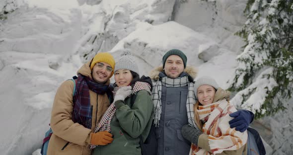 Portrait of Cheerful Millennials Smiling Looking at Camera in Winter Forest During Snow Fall