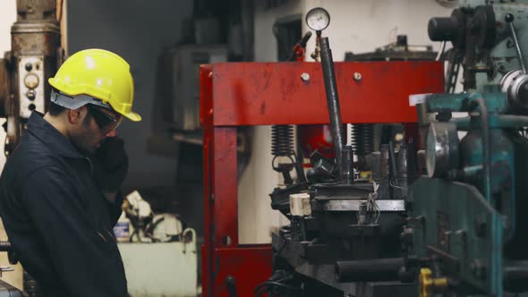 Factory Worker Talking on Portable Radio While Inspecting Machinery Parts