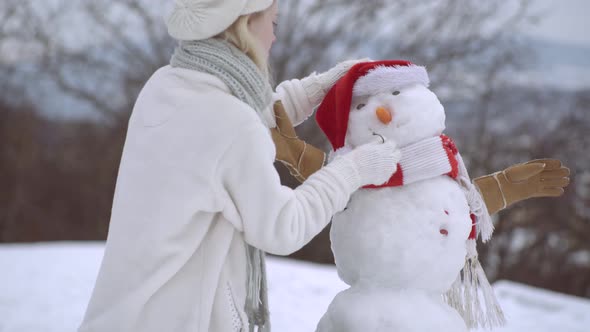 Happy Young Woman Having Fun in Winter. Snowman and Funny Girl. Make a Snow Man.