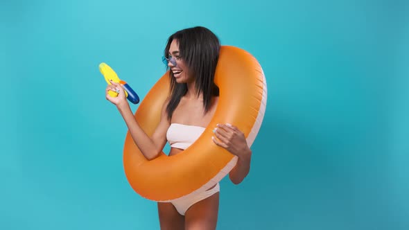 African Woman Dancing with an Inflatable Circle in a Swimsuit with a Water Gun in Her Hands Isolated