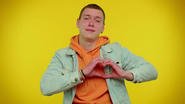 Smiling Teen Man Makes Heart Gesture Demonstrates Love Sign Expresses Good Feelings and Sympathy