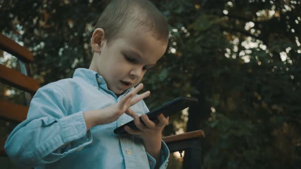 Little Boy Playing Video Games on His Smartphone Outdoors