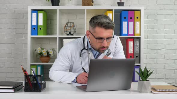 Doctor in hospital office looks magnifying glass, writes diagnosis in notebook