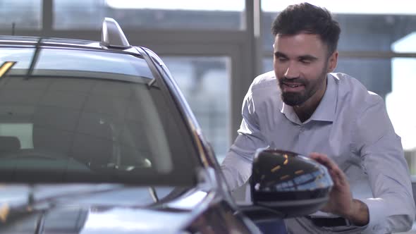 Happy Man Looking at Dream Car in Auto Showroom