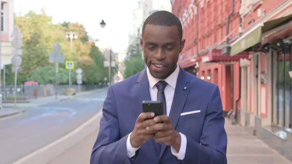 African Businessman Using Smartphone While Walking on Street