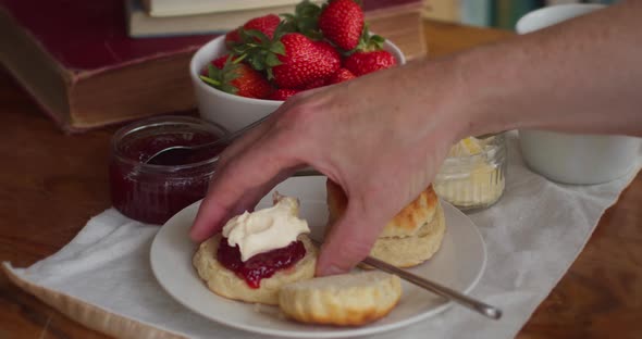 An Afternoon Tea with a Scone, Cream and Jam in Cornwall. Man Reaching for Scone with his Hand and E