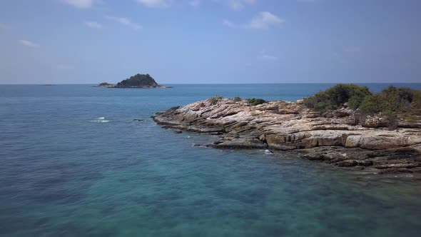 Aerial: A forward low altitude flight over azure transparent water and a rough rock formation, Andam