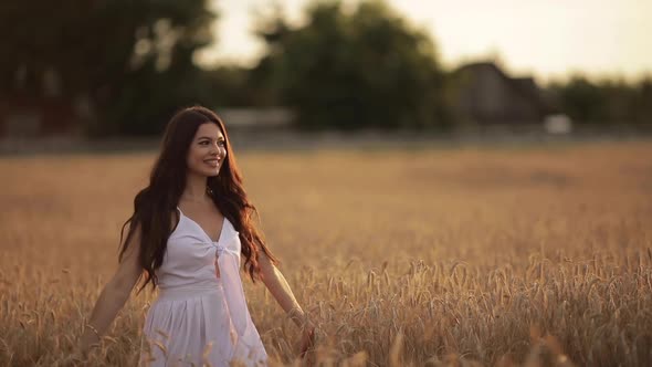 Beautiful Young Woman Enjoys Life Walking on a Wheat Field at Sunset