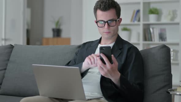 Young Male Designer Using Smartphone and Laptop at Home