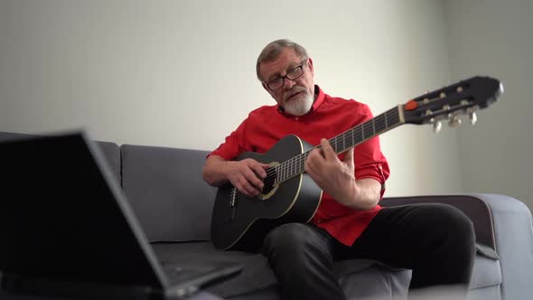 Elderly Man or Musician with Glasses and Red Shirt with Laptop Computer Learning To Play Guitar with