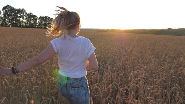 Dolly Shot of Happy Girl with Blonde Hair Running with Her Dog on Golden Wheat Field at Sunset