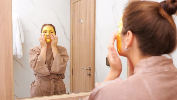 Woman with Golden Mask Does Face Massage at Hotel Mirror