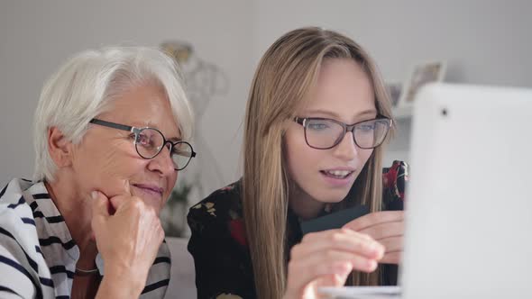 Granddaughter Helping Her Grandmother To Do Online Shopping. Ordering Goods Online