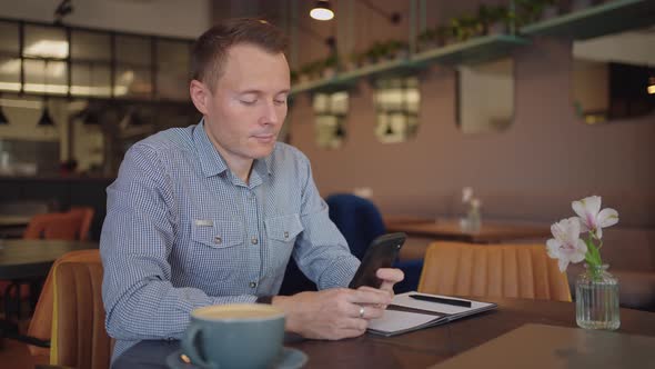 Medium Shot of Young Man Wearing Streetwear Sitting in Restaurant or Cafe in Front of Laptop and