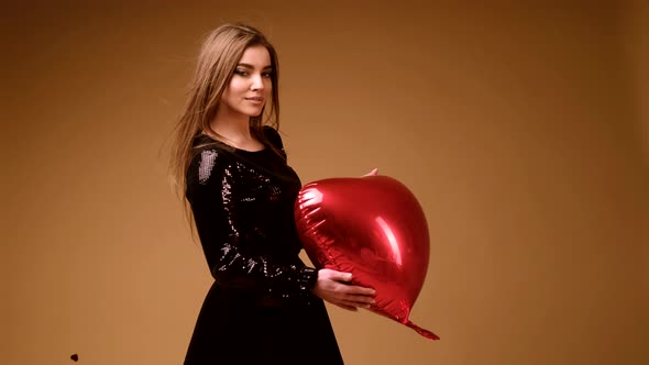 A Girl in a Black Dress with a Big Red Heart in Her Hands Rejoices on an Orange Background