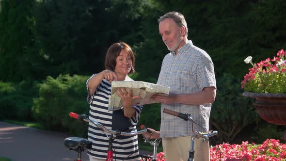 Senior Couple Talking About Routes for Bicycle Walking in Park.