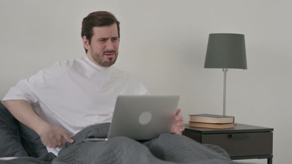 Young Man with Back Pain Working on Laptop in Bed