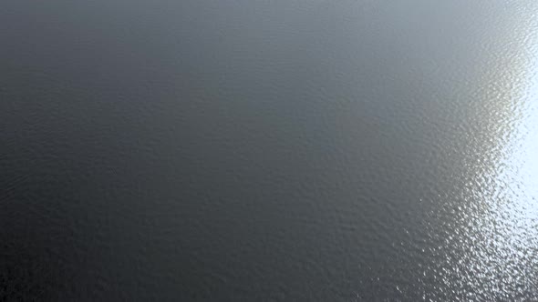 Drone flying low and fast along surface of rippled water with sunlight reflections.