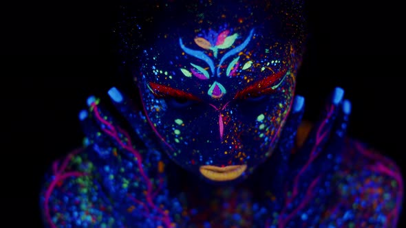 Woman with body art made with luminous fluorescent paints, open eyes and looks into camera