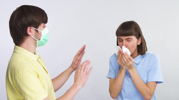 Sick Woman Coughing Into Tissue and Man in Protection Mask Showing Stop Sign To Her