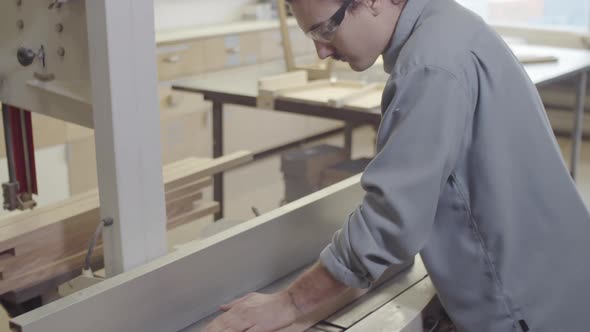 Young Carpenter Trimming Wood Board on Jointer Lathe at Workshop