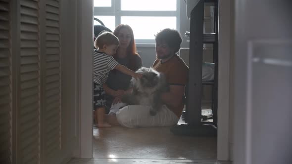 Happy Family Sitting on the Floor and Their Fluffy Cat Comes to Them