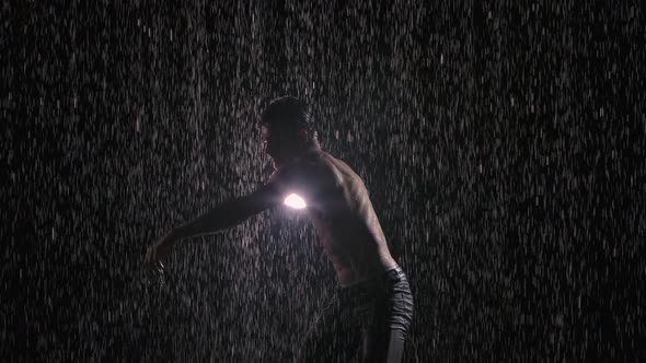 A Man with a Naked Torso Moves and Dances Sexually. Silhouette on a Black Background Under Streams