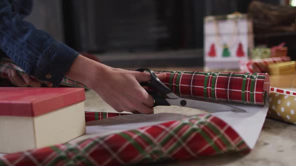 Mid section of woman cutting wrapping paper for Christmas presents at home