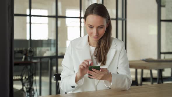 Excited Woman Celebrates Success By Holding a Mobile Phone in Her Hands While Sitting at a Desk in