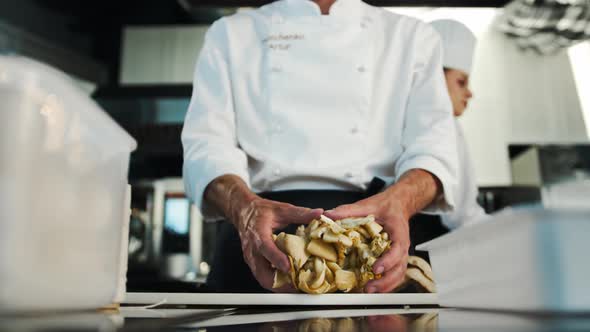 Professional kitchen, close-up: The chef cuts mushrooms, prepares a delicious dish in the restaurant