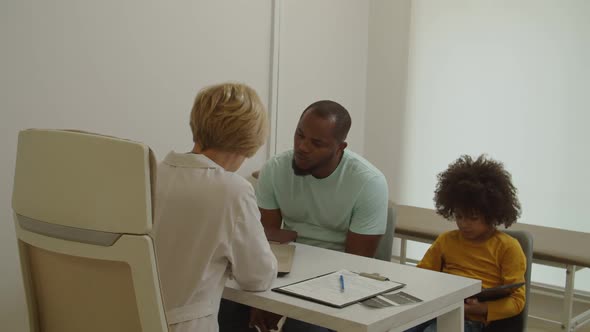 Professional Woman Doctor Explaining Medical Treatment to Worried Black Dad During Visit at Hospital