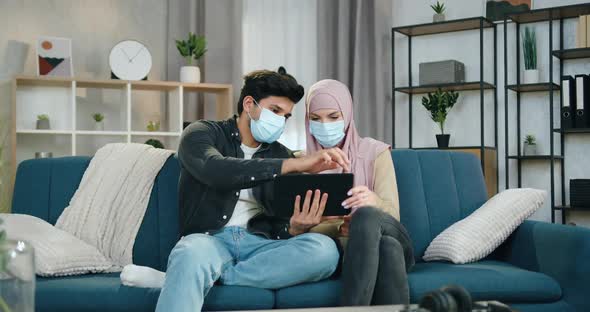 Arabian Couple in Medical Masks Sitting at Home During Isolation During Pandemia and Use Tablet PC
