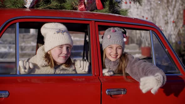 Two Smiling Teen Girl Looking To Camera and Waving Hands From Red Car Window. Playful Young Girl in