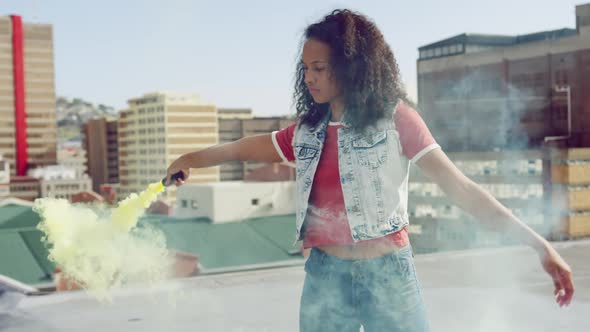 Fashionable young woman on urban rooftop using a smoke grenade