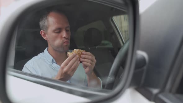 Man Eating an Hamburger While Driving His Car