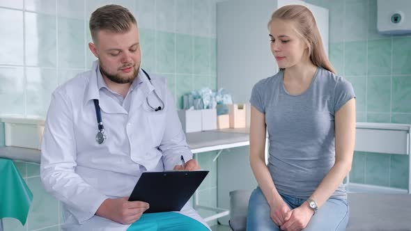 Young Attractive Male Doctor Talking with Female Patient at Hospital or Medical Office