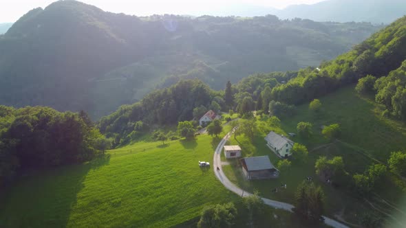 Flying over a small farm atop of a hill in scenic Valley in Slovenia. Idyllic rural landscape in fal