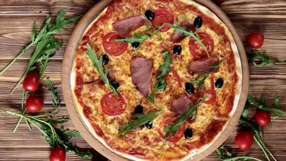 Italian pizza with ham, tomatoes, olives and basil on wooden table. Top view.