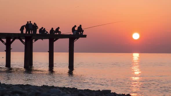 Silhouettes of Fishermen with Fishing Rods at Sea Sunset Sitting on the Pier, Slow Motion