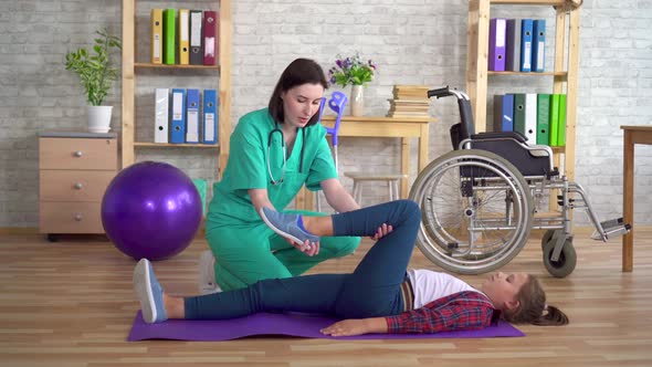 Physiotherapist in the Rehabilitation Center Helps in Warming Up the Legs of a Teenage Girl in