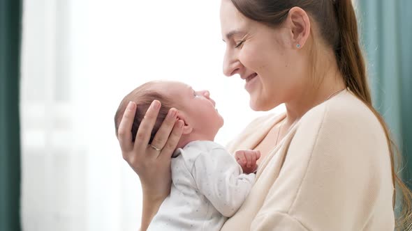 Portrait of 2 Weeks Old Little Baby Boy with Young Caring Mother Against Big Window at House