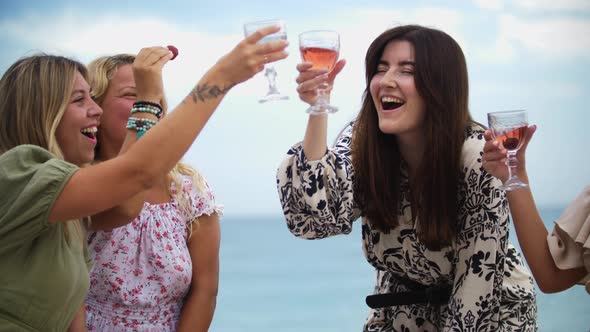 Four Smiling Women Clink Glasses of Alcohol on the Beach