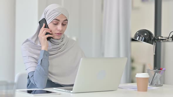 Young Arab Woman with Laptop Talking on Smartphone