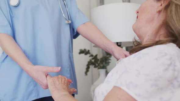 Female health worker holding hands of senior woman at home